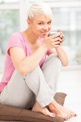 Smiling woman with mug sitting at home while smiling