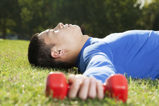 Young Athletic Man Lying Down in Park with Dumbbells