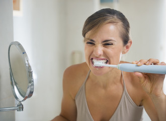 Young woman brushing teeth with grimace on face
