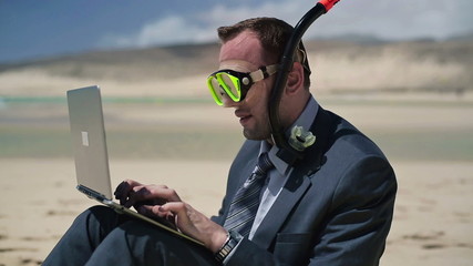 Businessman in diving mask working on laptop on the beach - Powered by Adobe