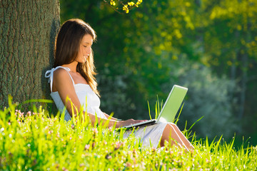 Beautiful young woman relaxing on grass with laptop