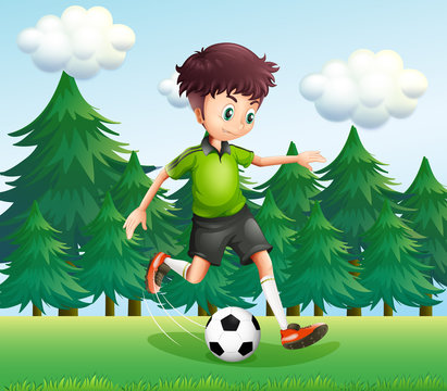 A boy kicking a soccer ball near the pine trees