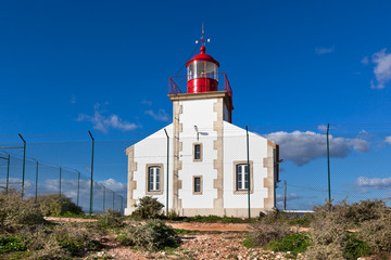 Fototapeta na wymiar Bright Lighthouse beyond chain link fence
