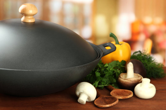 Black wok pan and vegetables on kitchen wooden table, close up