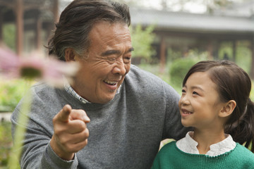 Grandfather and granddaughter looking at flower in garden