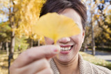 Mature Woman Covering Her Eyes with Yellow Ginkgo Leaf