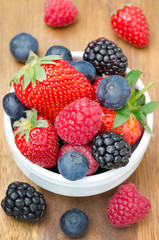 fresh berries in a white bowl on a wooden background