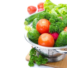 Fresh vegetables and herbs in metal colander, isolated