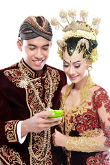 happy traditional java wedding couple with mobile phone