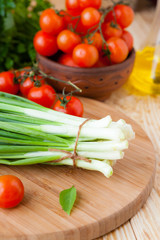 bunch of green onions on a cutting board and small tomatoes