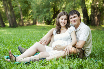 Pregnant wife and her husband on green grass
