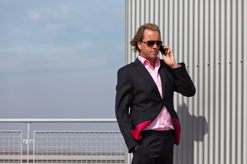 Business man with sunglasses calling near industrial wall.