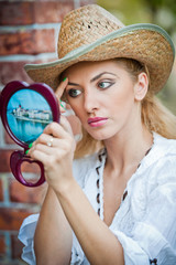 Young blonde woman looking in cosmetic mirror 