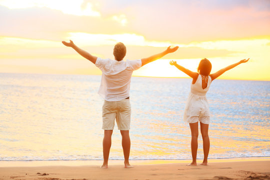 Happy cheering couple enjoying sunset at beach