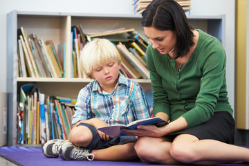 Elementary Pupil Reading With Teacher In Classroom