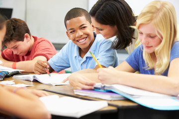 Teacher Helping Pupils Studying At Desks In Classroom