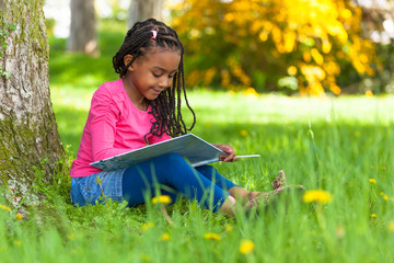Outdoor portrait of a cute young black little girl reading a boo - 52160502