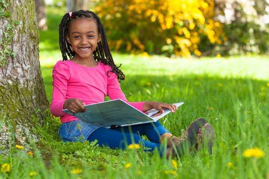 Outdoor portrait of a cute young black little girl reading a boo