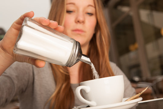 Junge Dame gie&szlig;t Zucker in Kaffee Tee Tasse