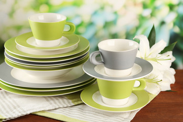 Empty plates and cups on wooden table on green background