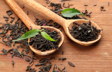 Dry tea with green leaves in wooden spoons, on wooden