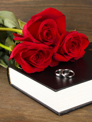 Wedding rings on bible with roses on wooden background