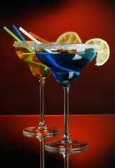 Yellow and blue cocktails in glasses on color background