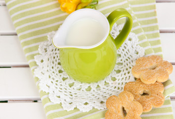 Green jug with milk and cookies on wooden picnic table close-up