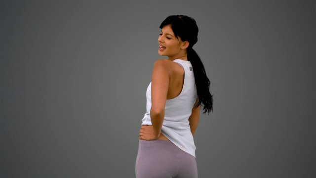 Fit brunette turning and smiling on grey background