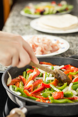 Closeup of female cooking vegetables and chicken in a pan