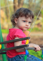 Cute child girl swinging and looking serious on summer backgroun