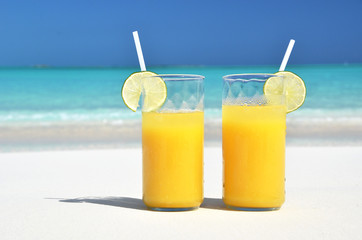 Two glasses of orange juice on the sandy beach