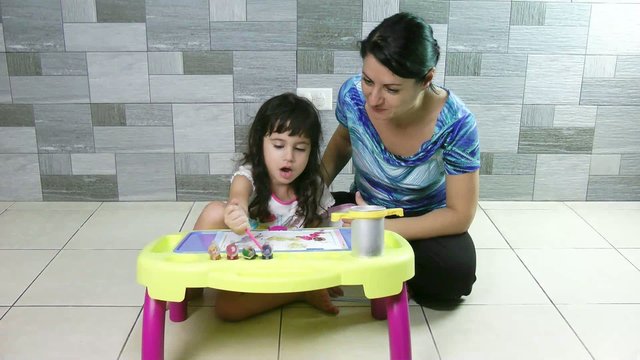 Mother teaching her little daughter to paint.