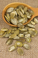 Shelled raw pumpkin seeds in wooden spoon on burlap