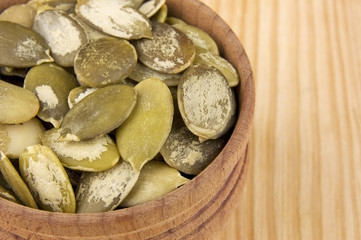 Shelled raw pumpkin seeds in wooden bowl close up