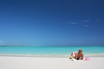 Fototapeta na wymiar Girl with a glass of orange juice on the beach of Exuma, Bahamas