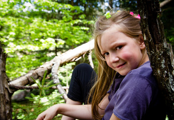 Pretty little girl sitting on the stump in the forest and posing
