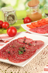Tasty salami on plates on wooden table on natural background
