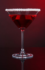 Red cocktail in martini glass on dark red background