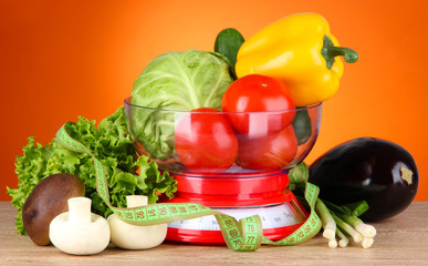 Fresh vegetables in scales on table on orange background