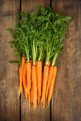 fresh carrots with green leaves over wooden
