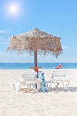 Wooden beach umbrella and sun bed on the beach, in the backgroun