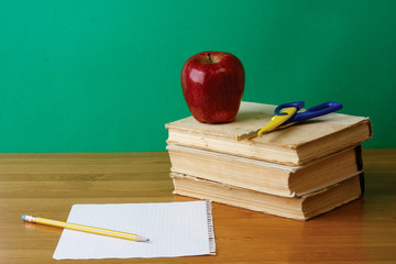 Red apple on a pile of books, paper and pencil on the desk