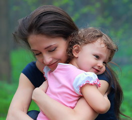 Smiling happy mother and cute kid girl cuddling outdoor summer b