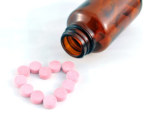 Heart shape pills outside a bottle on white background