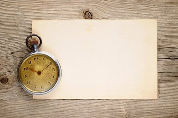 Vintage pocket watch and old postcard on wooden background