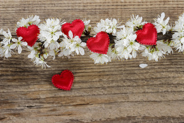 Small red hearts among cherry blossom on wooden background