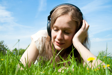 Beautiful young woman listening music laying in the grass