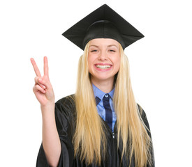 Happy young woman in graduation gown showing victory gesture