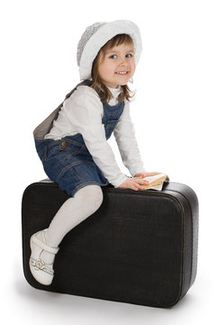 Smiling little girl sitting on a suitcase with small book